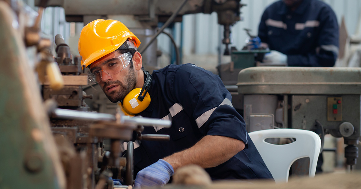 Un trabajador manipula una máquina en su puesto de trabajo mientras inclina su cuerpo hacia el lado derecho 