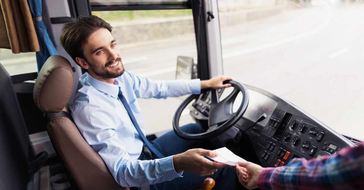 Un conductor de autobús sonríe mientras coge el billete de un pasajero