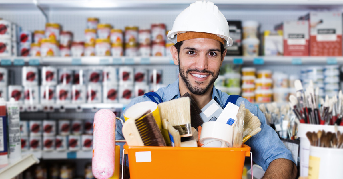 Vendeur souriant dans un commerce de détail non alimentaire tenant un panier d’outils