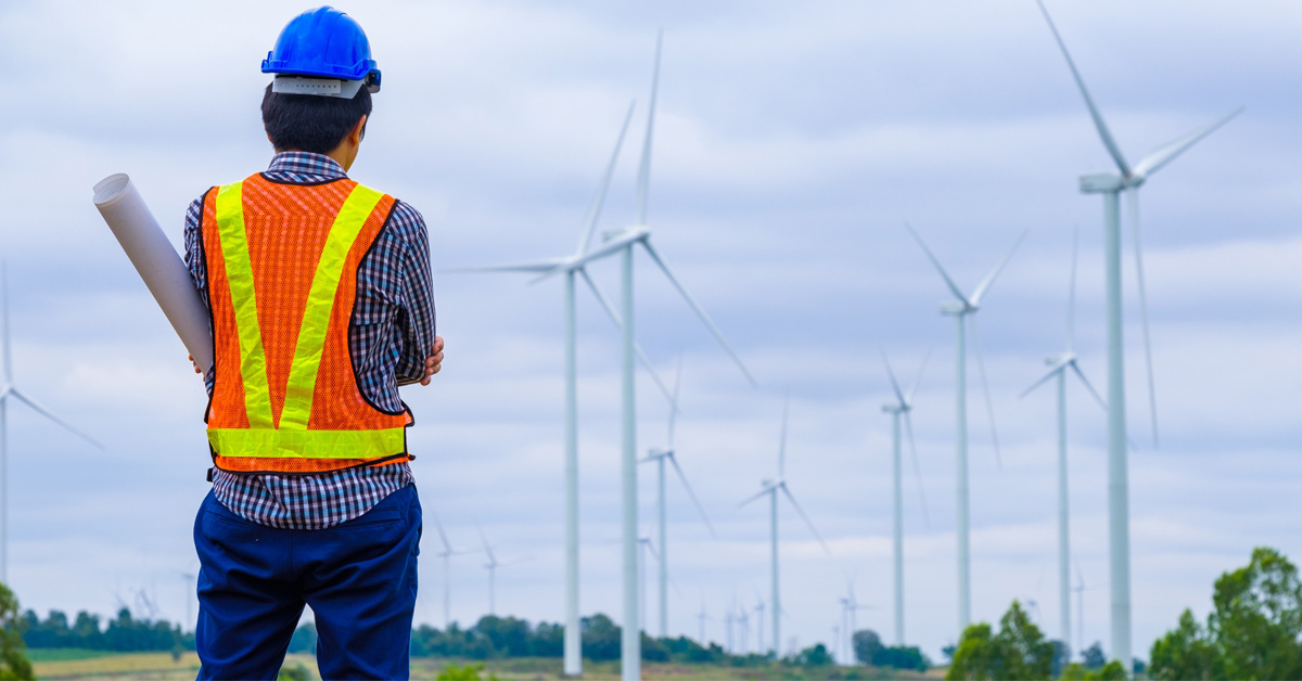 Homme de dos avec un casque et un gilet de sécurité et éoliennes en arrière-plan