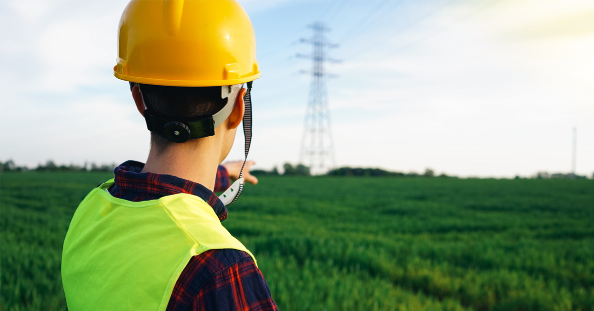 Travailleur de dos avec un casque de sécurité et pointant du doigt une tour à haute tension