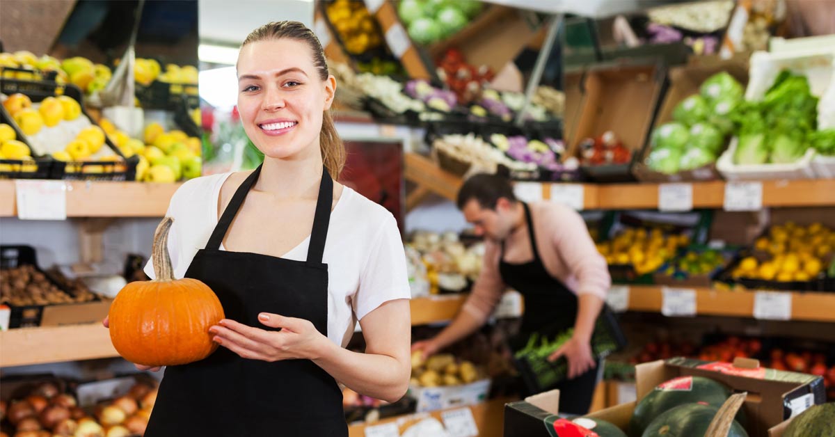 Vendeuse du secteur du commerce de détail en premier plan qui organise les fruits et les légumes du magasin