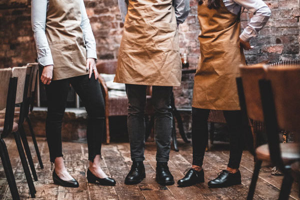 Three waitstaff are standing in restaurant wearing different, black-coloured non-slip shoe styles