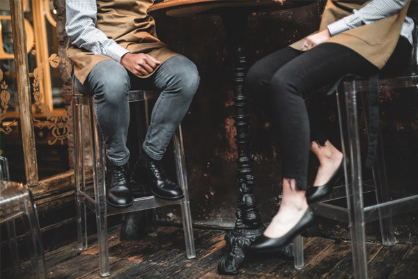 Two restaurant servers taking a seated break on bar stools wearing black slip-resistant shoes