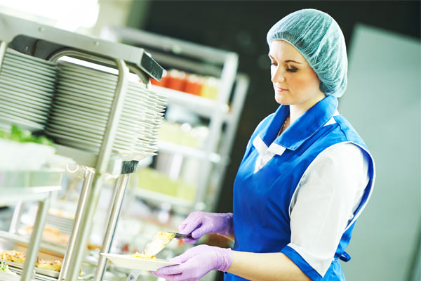 Hospital cafeteria worker serving food while wearing PPE gloves and hair covering