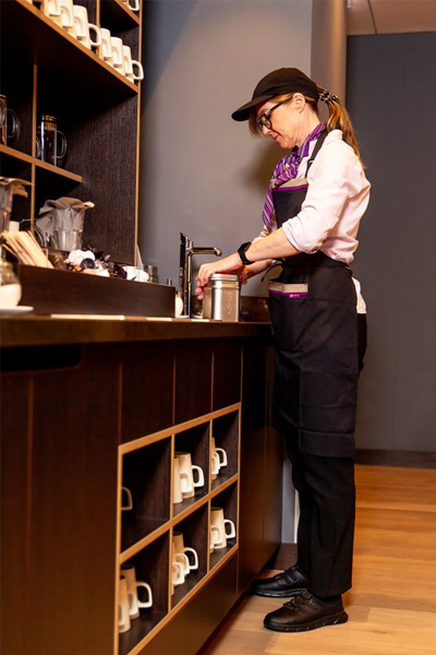 Kitchen staff worker cleaning metal tins at a sink wearing black, slip-resistant shoes