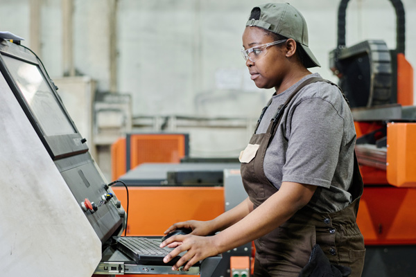 Female worker in protective glasses looking at computer monitor while controlling machine