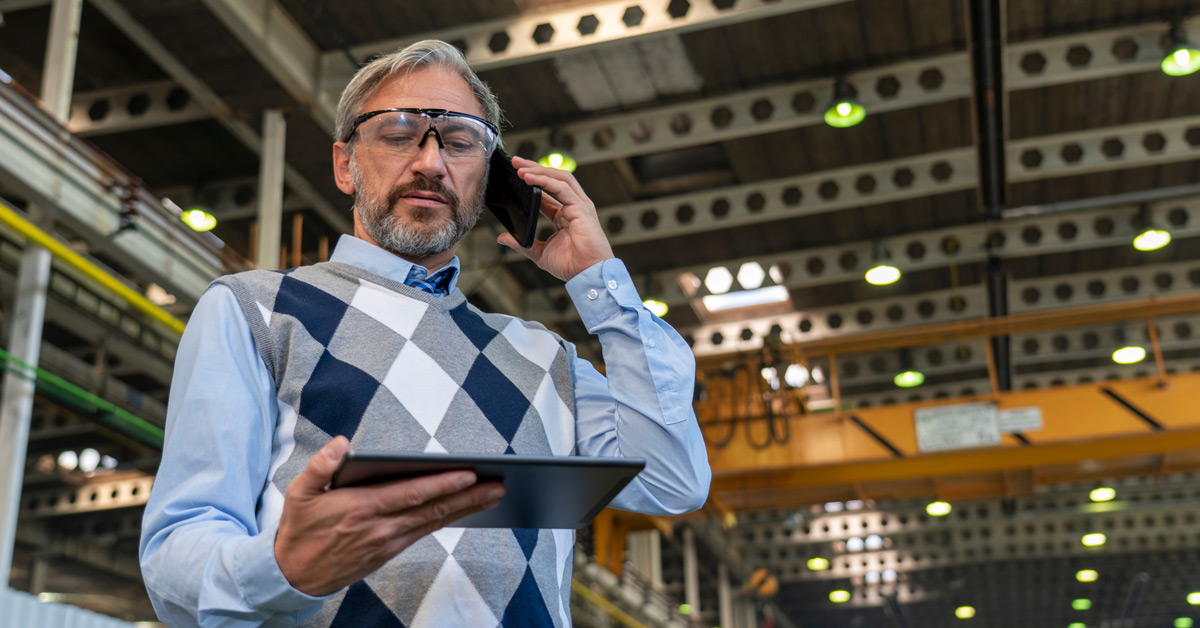 Manager looking at a tablet while talking on the phone in a manufacturing facility