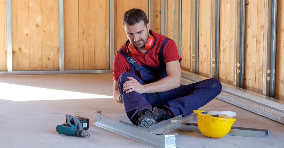 Construction worker sitting on floor holding his knee after suffering an injury