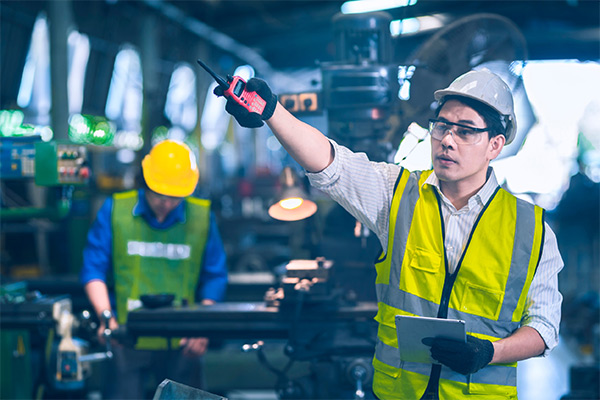 Supervisor wearing safety gear, holding tablet and pointing with a radio in hand