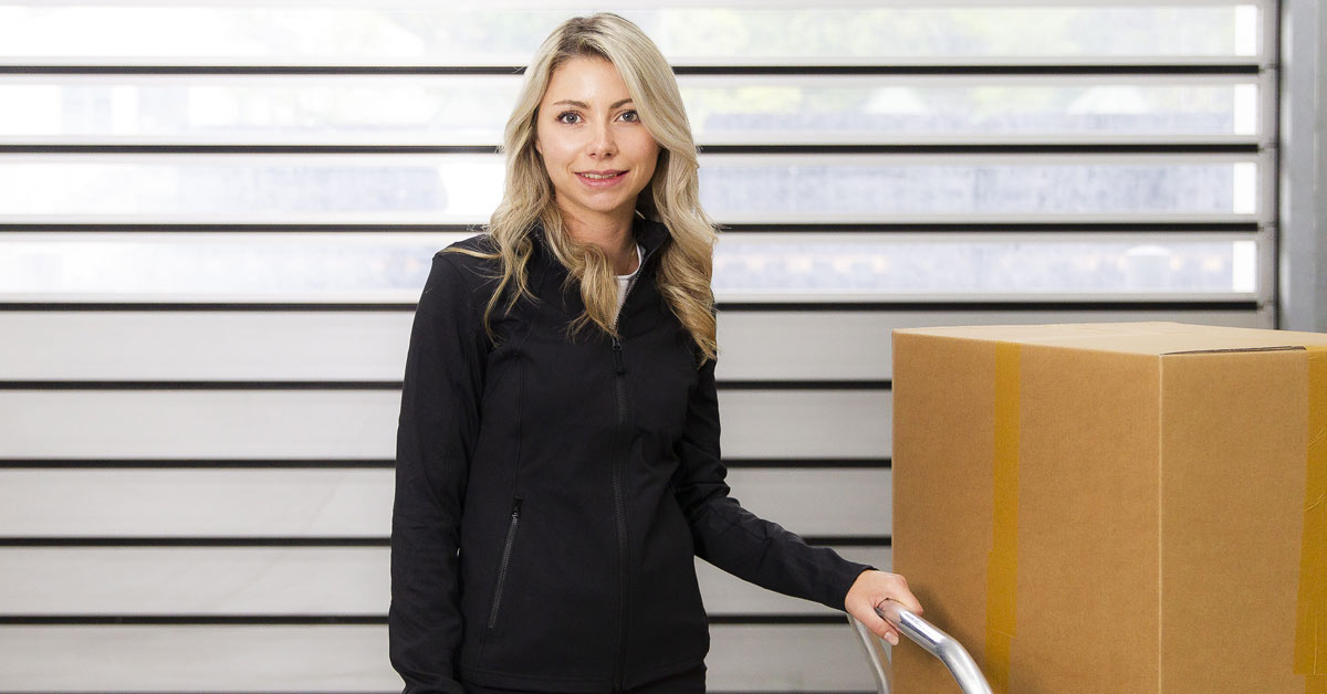 Parcel courier standing next to stacked boxes on dolly