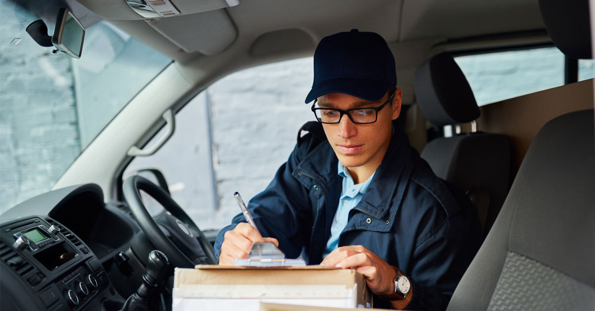 Delivery driver writing on a clipboard on top of a box inside van